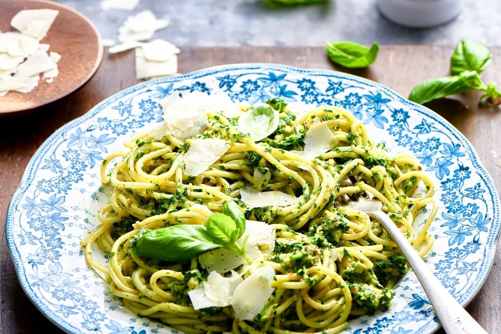 Spaghetti mit grünem Pesto, Parmesanspänen und Basilikum auf einem blau-weiß gemusterten Teller