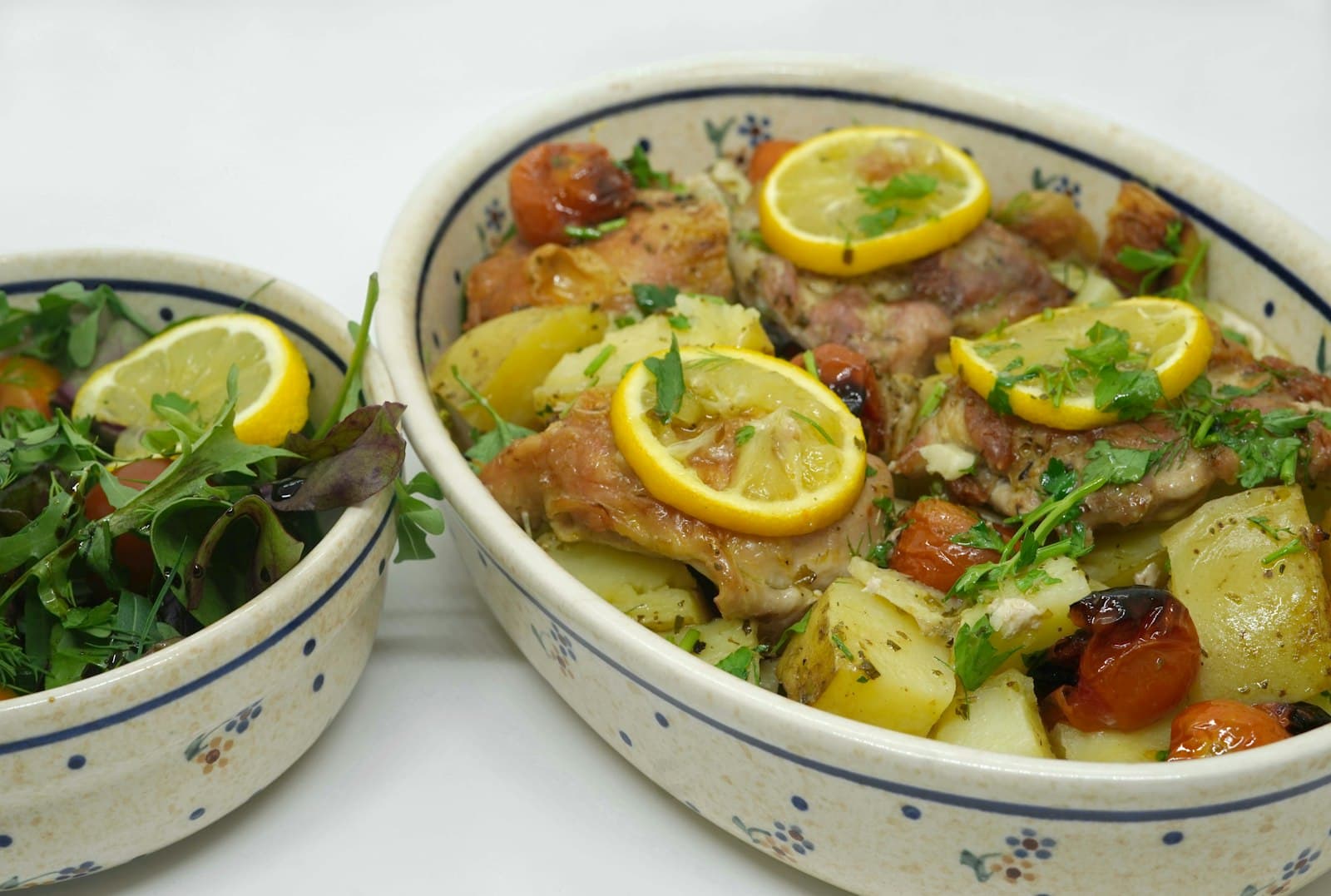 Ofenhähnchen mit Zitronenscheiben, Kartoffeln, Kirschtomaten und Petersilie in einer Auflaufform, daneben eine Schale Blattsalat